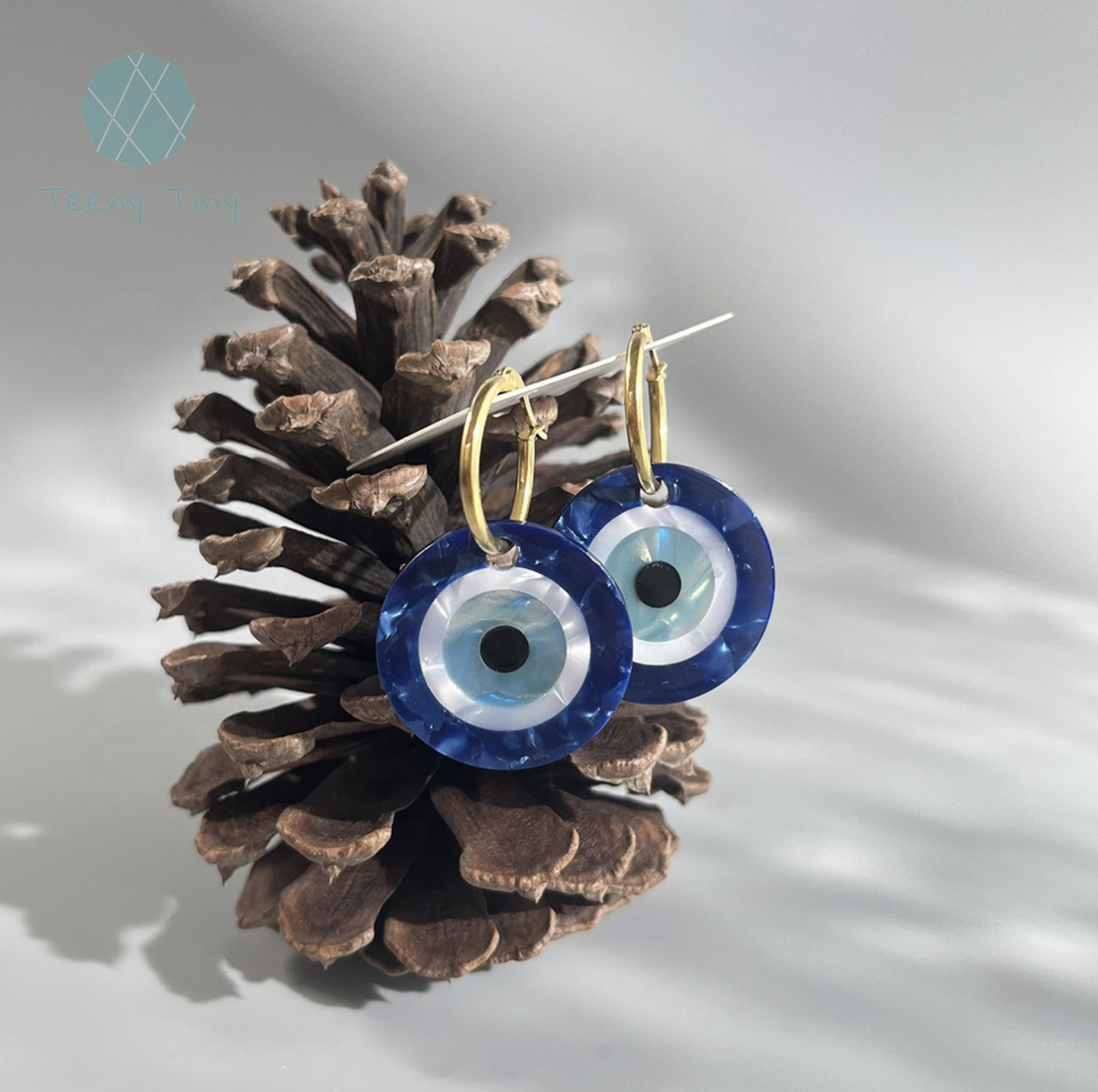 two blue evil eye glass earrings in a pine cone