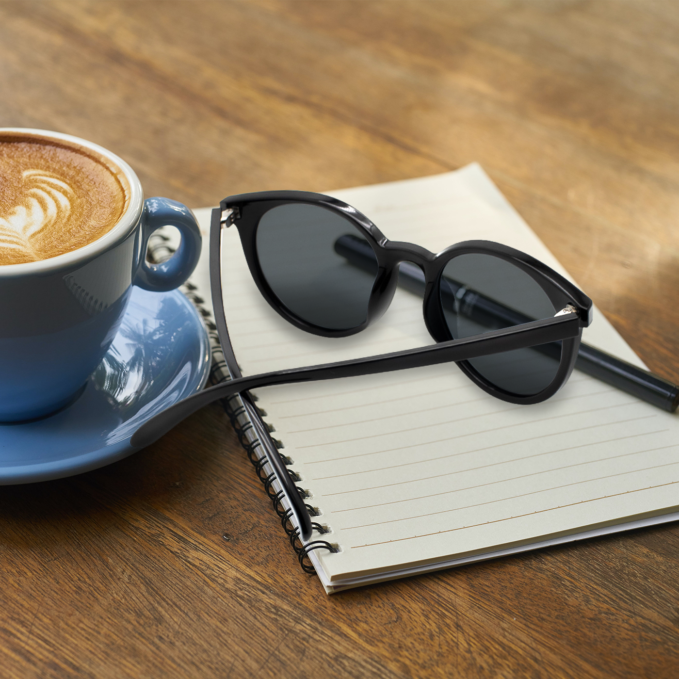 Black sunglasses featuring a gold aquarius zodiac sign engraved on the endpiece - flat lay coffee and table