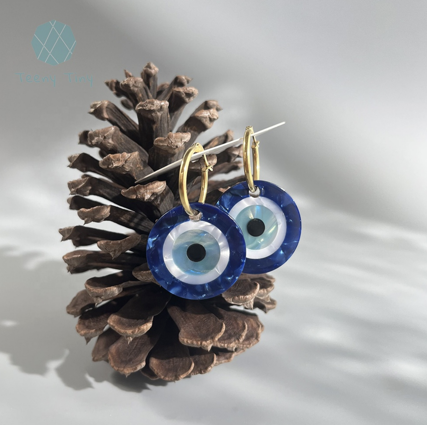  two blue evil eye glass earrings in a pine cone